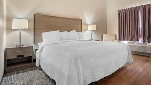 A hotel room with a large bed, bedside lamps, a chair, and a window with curtains. - Red Roof Inn PLUS+ & Suites Vicksburg (Vicksburg)