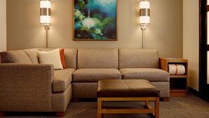 A modern living room with a sectional sofa, a wooden bench, two wall-mounted lamps, and a framed abstract painting. - Hyatt Place Atlanta Downtown (Atlanta)