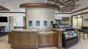 A hotel lobby with a central wooden reception desk, a seating area with chairs, and a coffee station with a glass display case. - Hyatt Place Atlanta Downtown (Atlanta)
