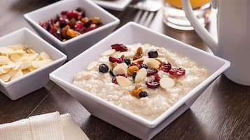 Une table mise pour le petit-déjeuner avec un bol de porridge garni d’amandes et de fruits rouges, un saladier de fruits secs et un verre de jus d’orange.