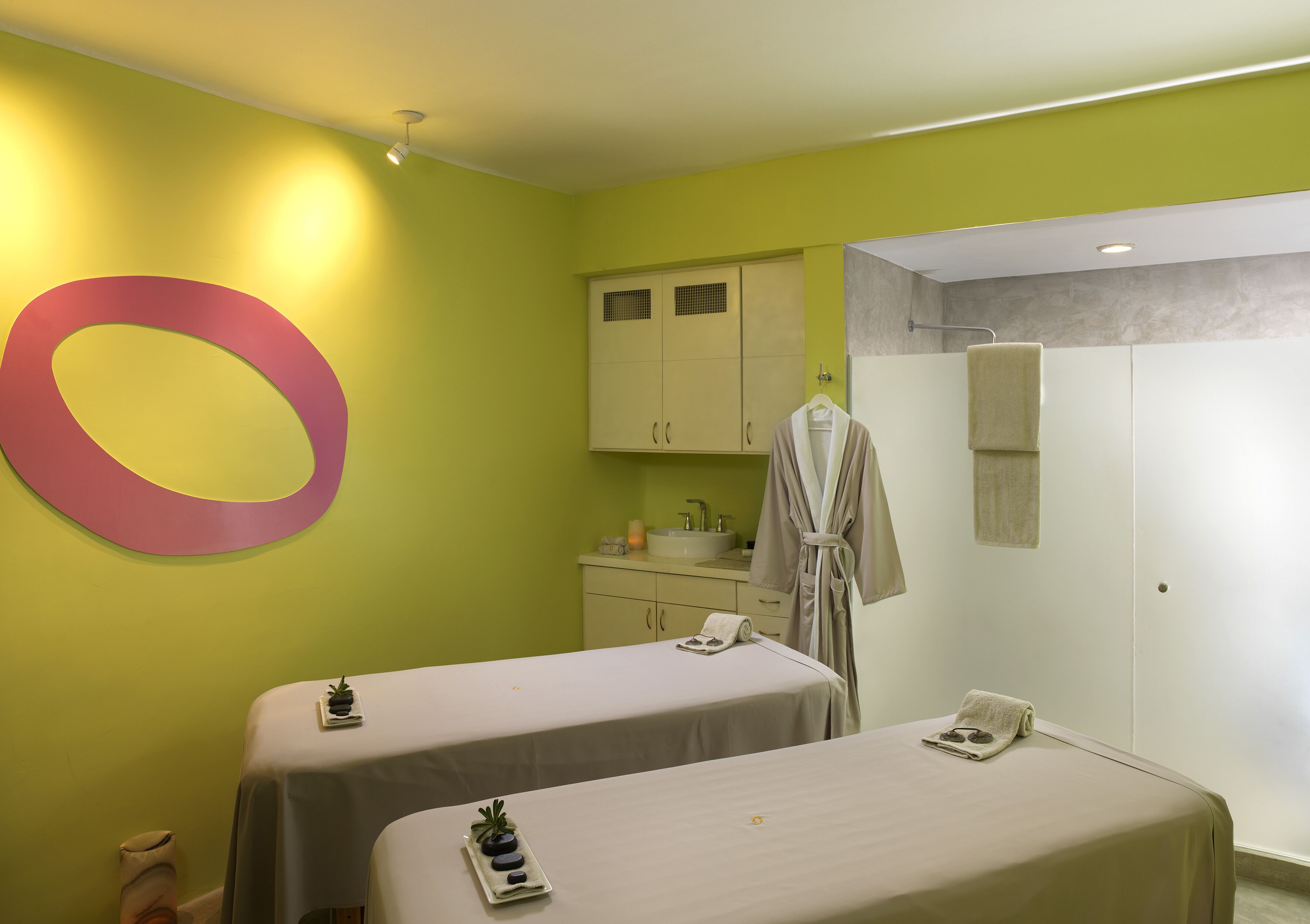 A room with two beds, a large wall decoration, a sink, and a robe hanging on the wall.