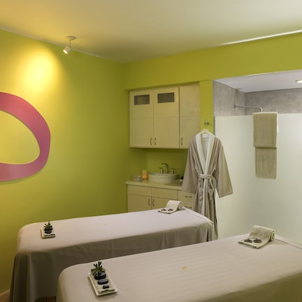 A room with two beds, a large wall decoration, a sink, and a robe hanging on the wall.