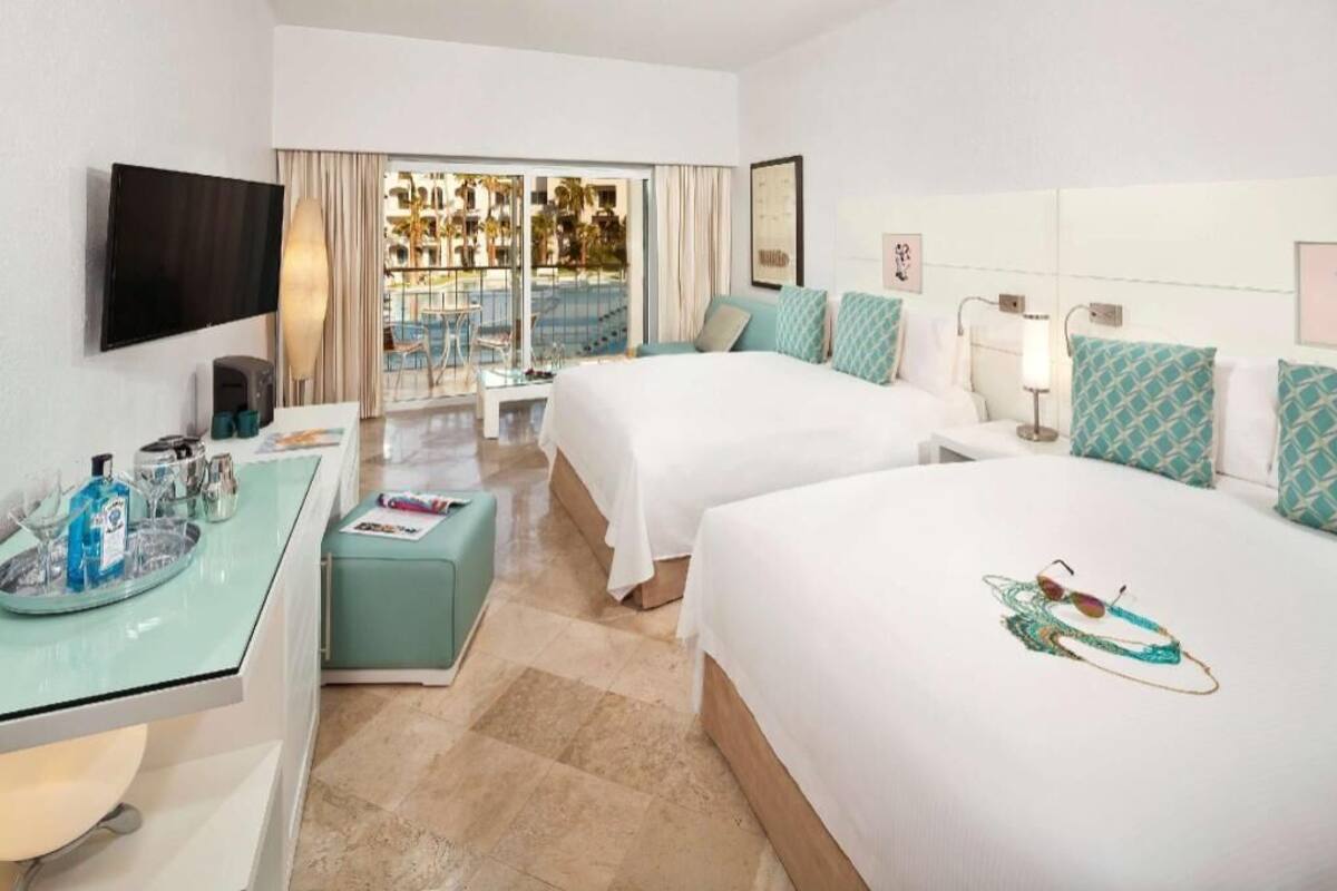 Habitación de hotel con dos camas, televisión, escritorio con superficie de vidrio y vistas a una piscina y zona exterior.
