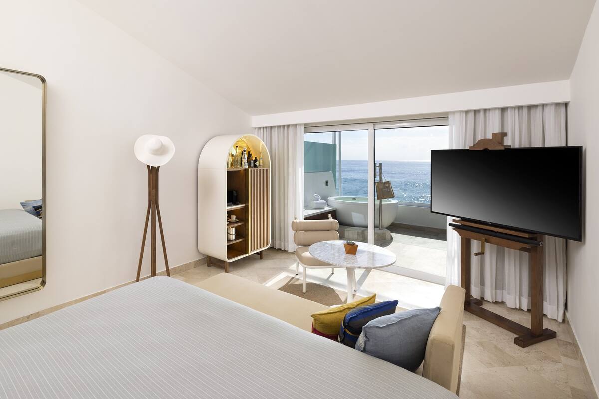 Habitación de hotel con cama, televisión, balcón y vistas al mar, además de un minibar.