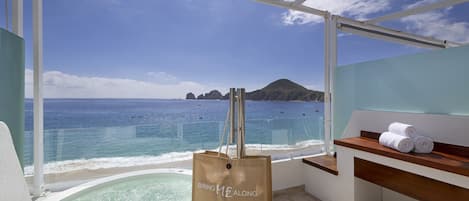 A balcony with a view of the ocean, a hot tub, and a towel rack.