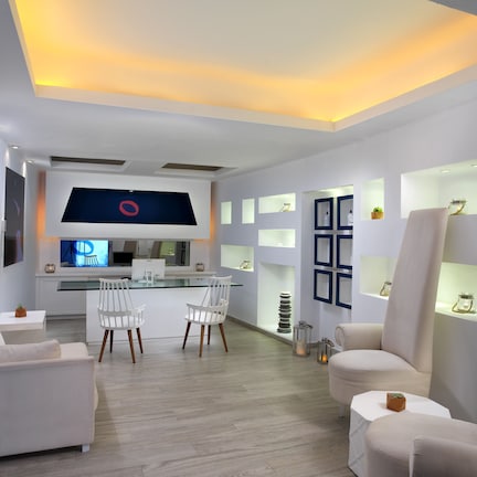 A modern, well-lit room with a large flat-screen TV, white furniture, and built-in shelves with decorative items.