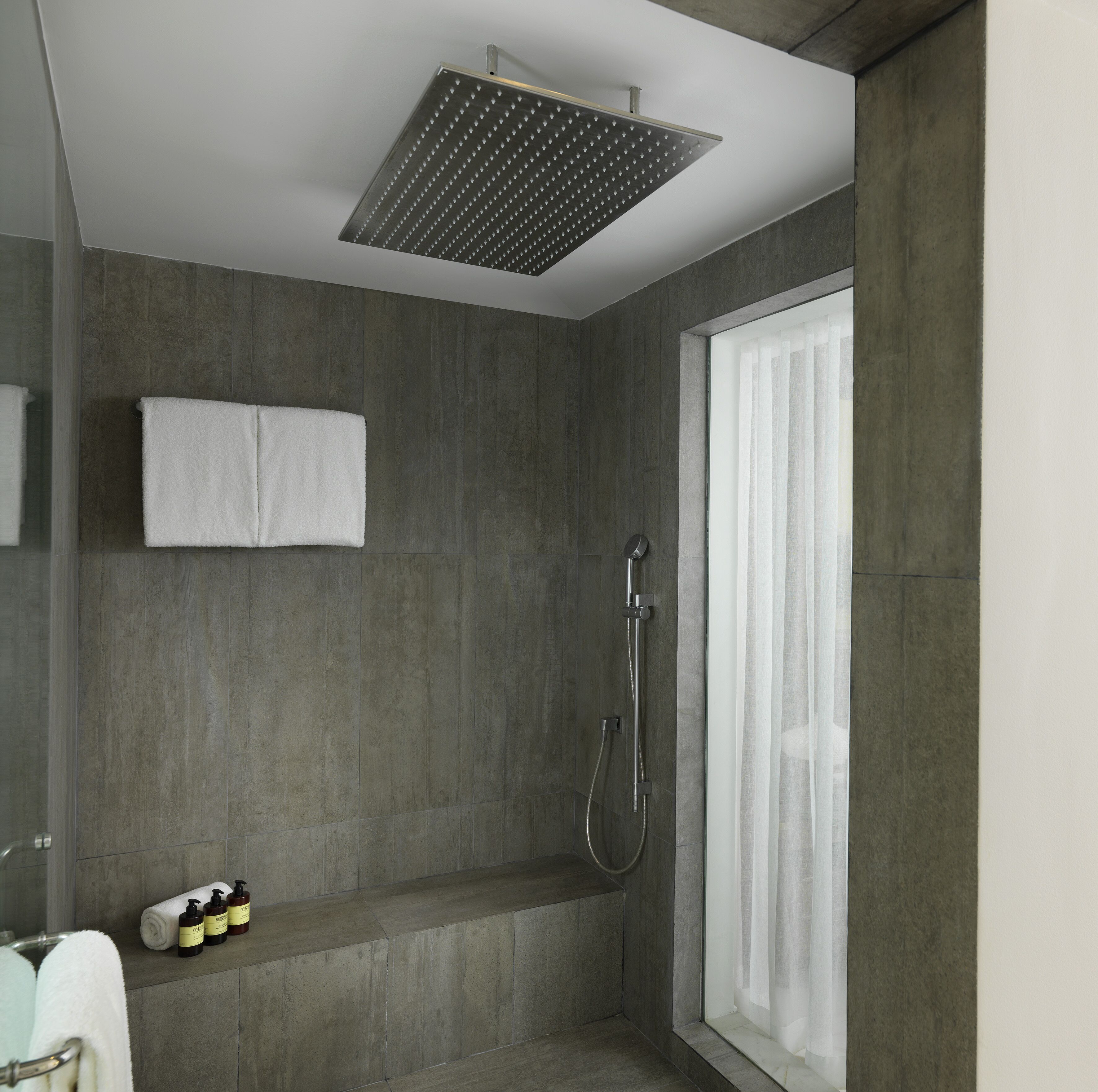 A modern shower room with a square showerhead, a glass shower enclosure, and a large window.