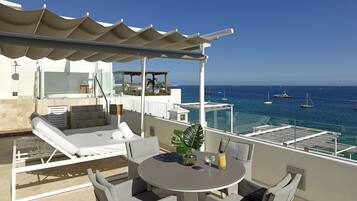 A rooftop terrace with a pool, lounge chairs, a table with drinks, and a view of the sea with boats.