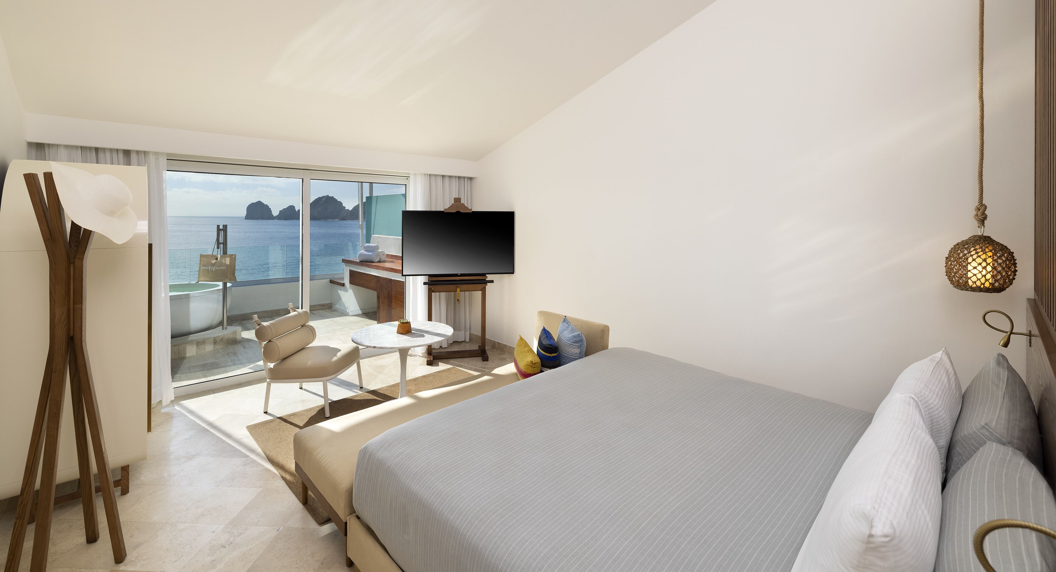 A hotel room with a bed, a TV, a desk, and a view of the sea.