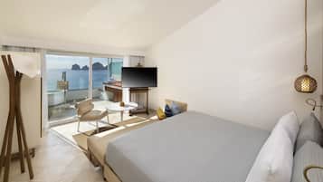 A hotel room with a bed, a TV, a desk, and a view of the sea.