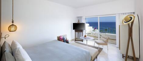 A hotel room with a bed, a TV, a balcony with a view of the sea, and a hat on a stand.