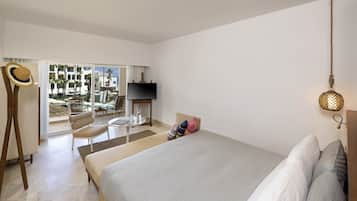 Een hotelkamer met een bed, een televisie, een tafel met stoelen en uitzicht op palmbomen en gebouwen.