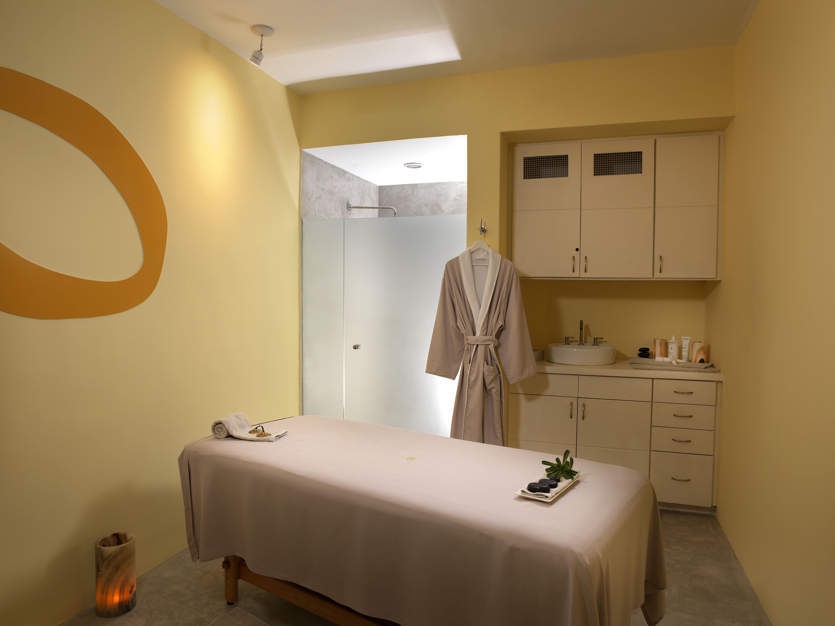 Um quarto de spa com mesa de massagem, um roupão pendurado, pia e armários.