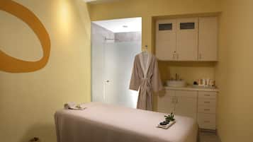Um quarto de spa com mesa de massagem, um roupão pendurado, pia e armários.