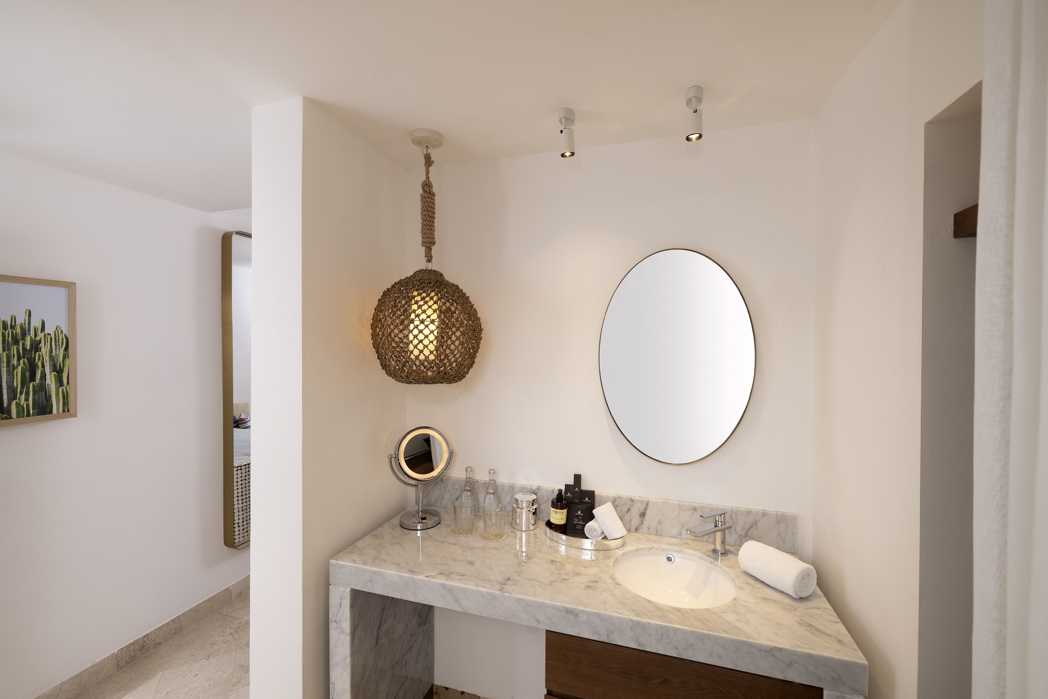 A bathroom with a marble sink, a round mirror, a hanging light fixture, and a framed picture on the wall.
