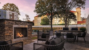 Un patio al aire libre con paredes de piedra, una fogata, muebles de mimbre y vistas a un edificio con techo rojo.