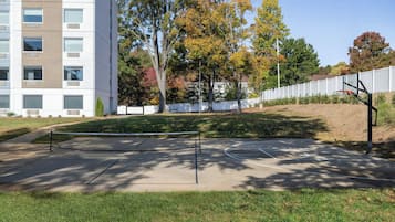 Una cancha de baloncesto al aire libre con valla, árboles y un edificio al fondo.