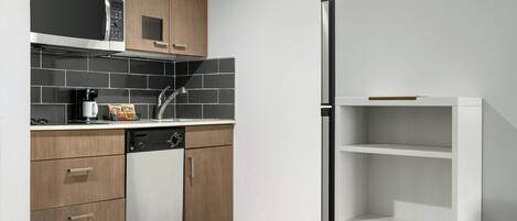 Una cocina moderna con armarios de madera, microondas integrado, lavavajillas y estantería blanca.