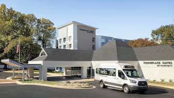 A modern hotel with a white exterior, a covered entrance, and a van parked in front.