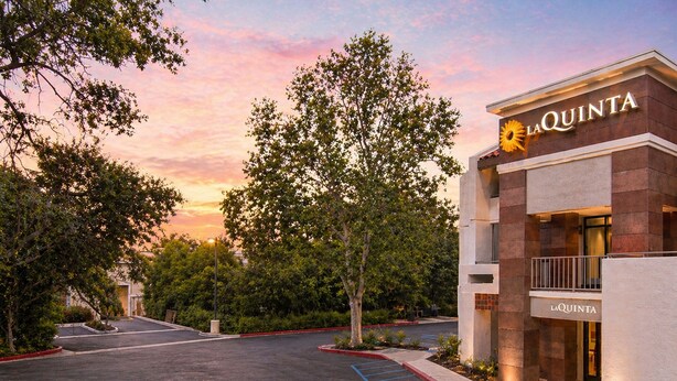 A hotel entrance with a parking lot, trees, and a sunset sky. - La Quinta Inn & Suites by Wyndham Thousand Oaks-Newbury Park (Thousand Oaks)