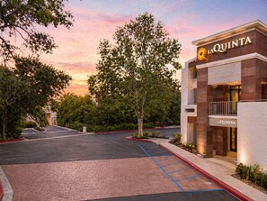 L’entrée d’un hôtel, avec un parking, des arbres et un ciel au coucher du soleil.