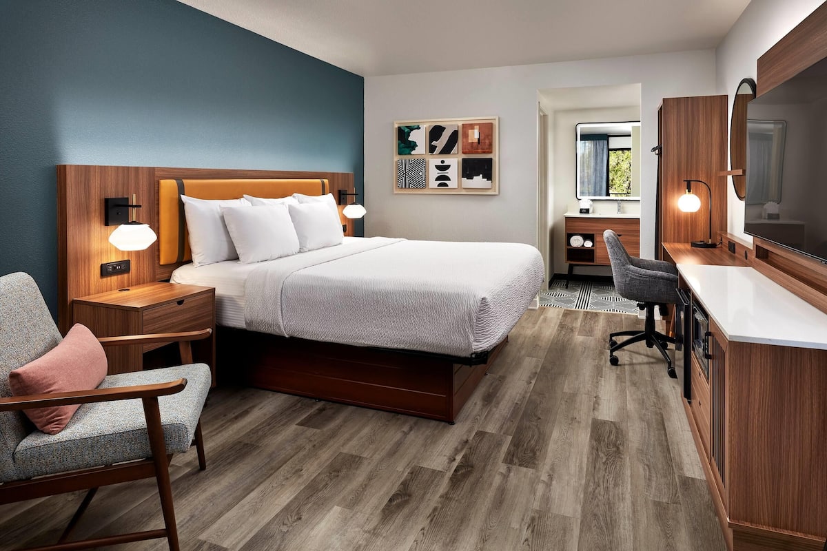 A modern hotel room with a large bed, a desk, a chair, and a TV.