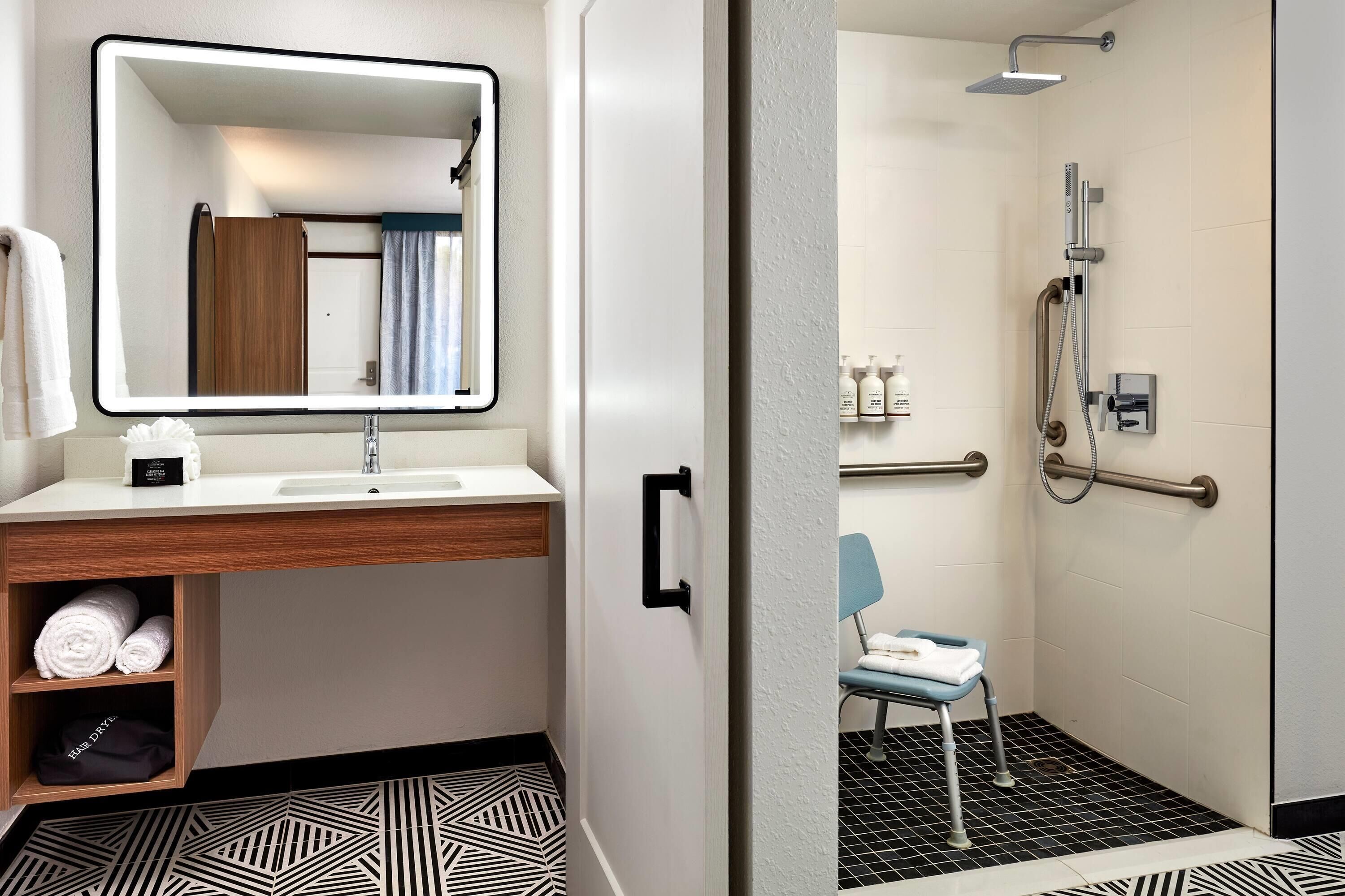 Un baño moderno con un espejo grande, un lavamanos, una ducha y una silla.
