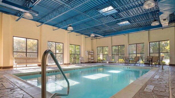 Piscina interior com água azul cristalina, chão de pedra e teto metálico azul.