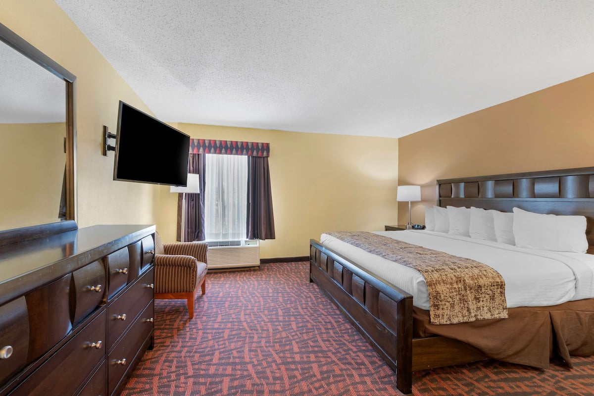A hotel room with a large bed, a dresser, a television, and a window with curtains.