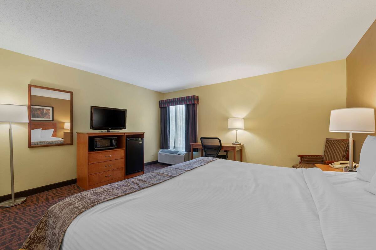 A hotel room with a large bed, a desk with a chair, a television, a microwave, and a small refrigerator.