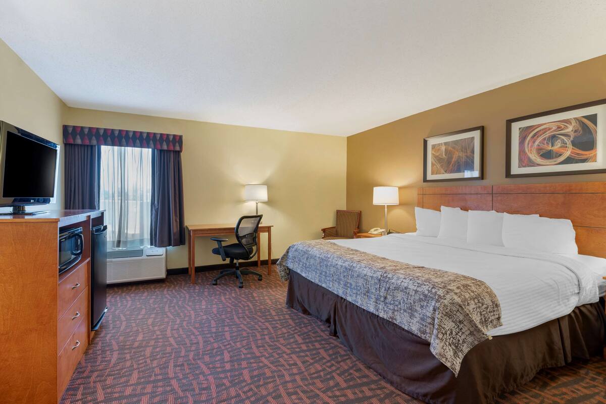 A hotel room with a bed, desk, chair, television, and a window with curtains.