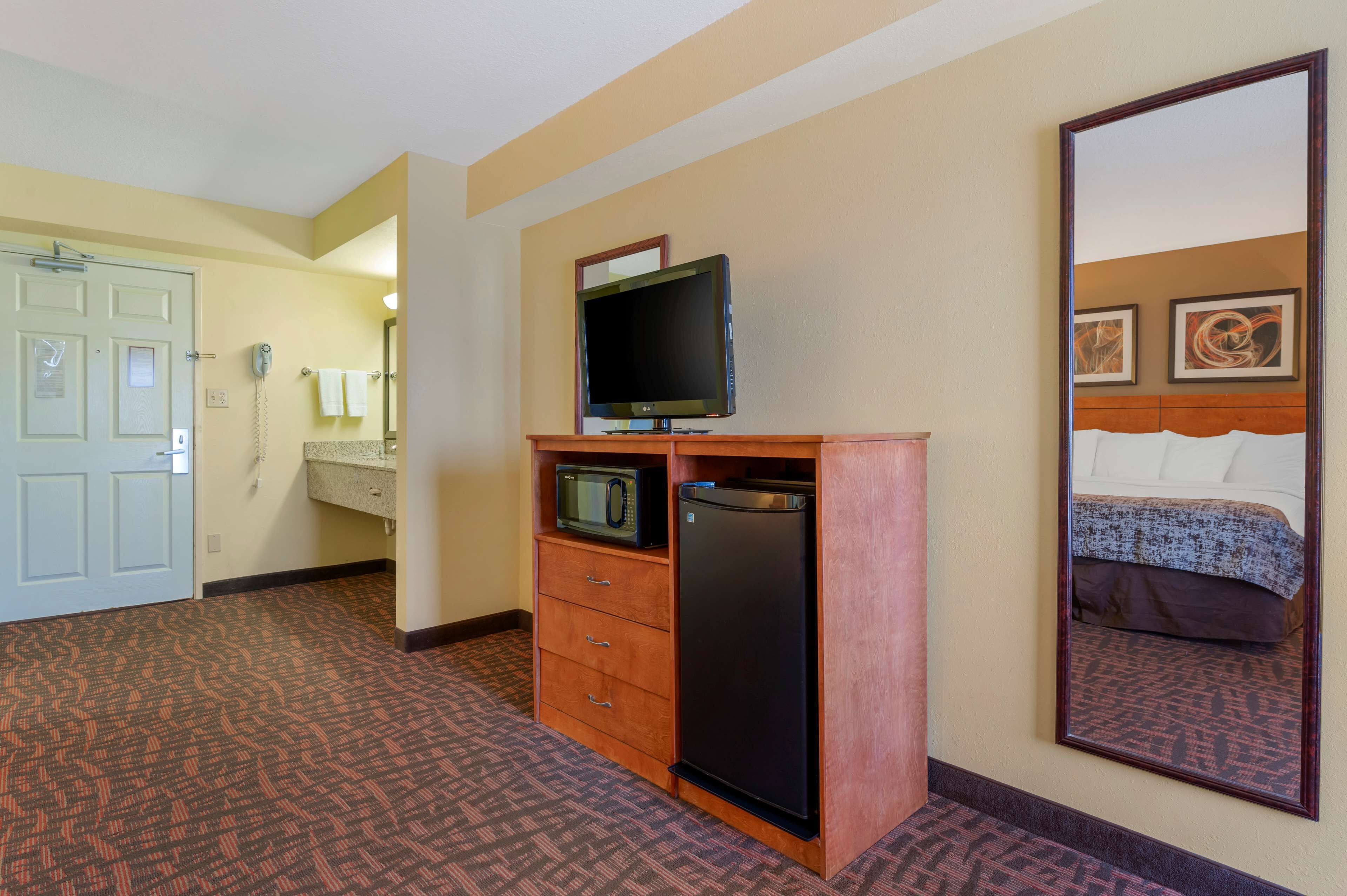 A hotel room with a bed, a television, a refrigerator, a microwave, and a telephone.