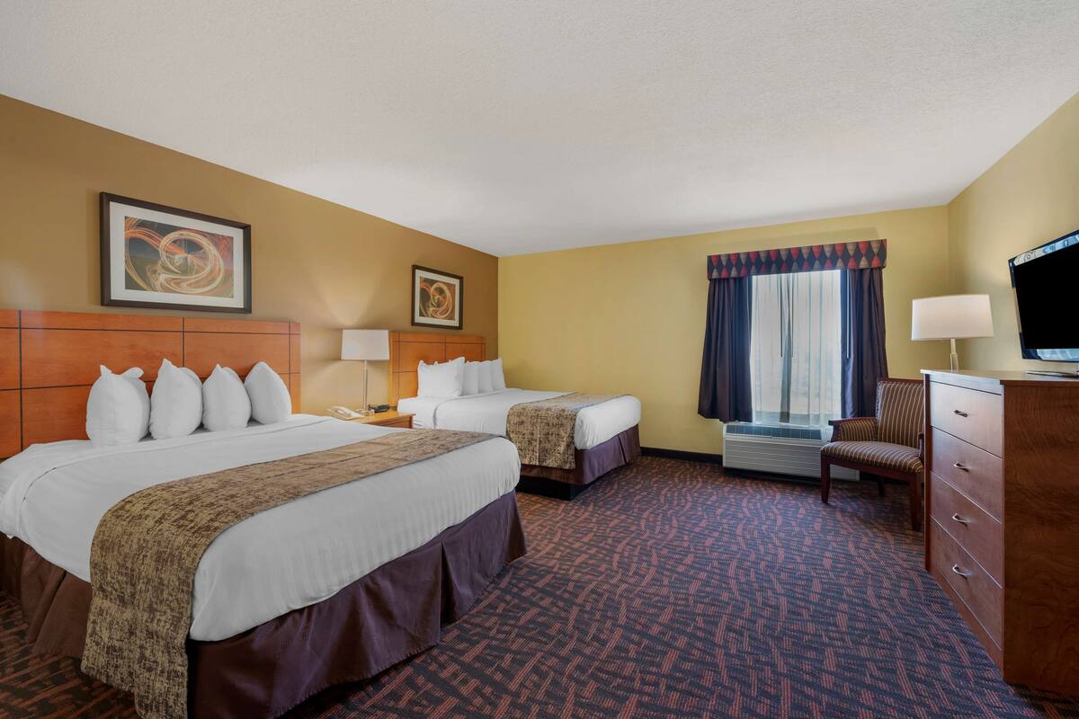 A hotel room with two beds, a desk, a chair, a TV, and a window with curtains.