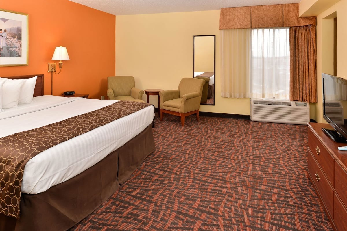 A hotel room with a bed, a desk, a chair, a television, and an air conditioning unit.