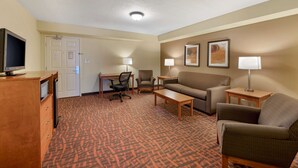 Quarto de hotel com escrivaninha, duas cadeiras, um sofá, televisão e um tapete estampado.