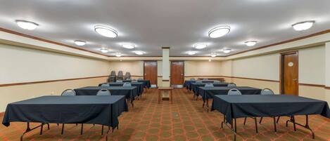 A conference room with multiple tables and chairs, carpeted floor, and ceiling lights.