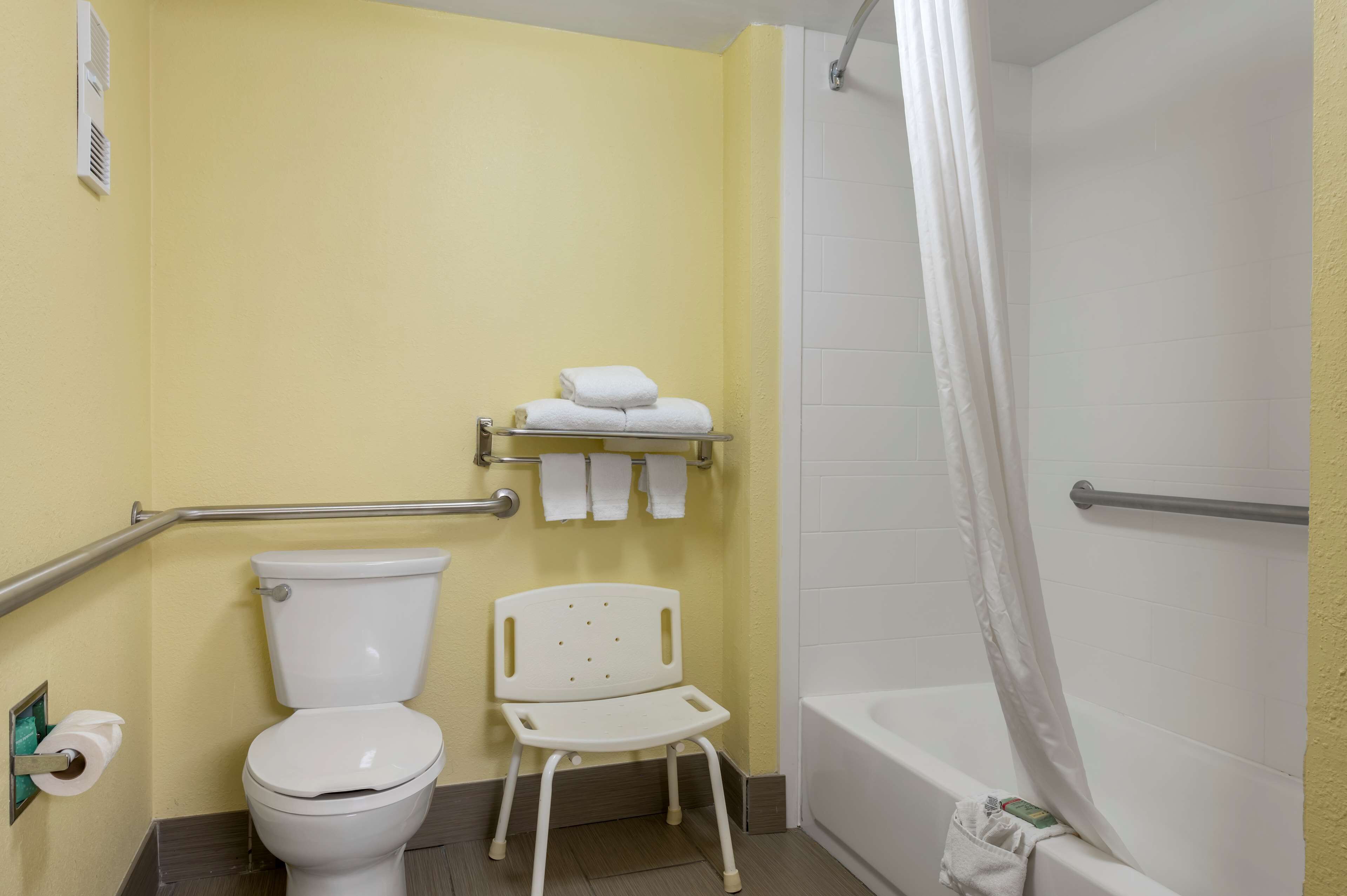 Un bagno con un water, una sedia bianca, uno scaffale con asciugamani e una vasca da bagno.