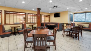 Restaurante com mesas e bancos de madeira, uma janela ampla com vista e uma TV de tela plana na parede.