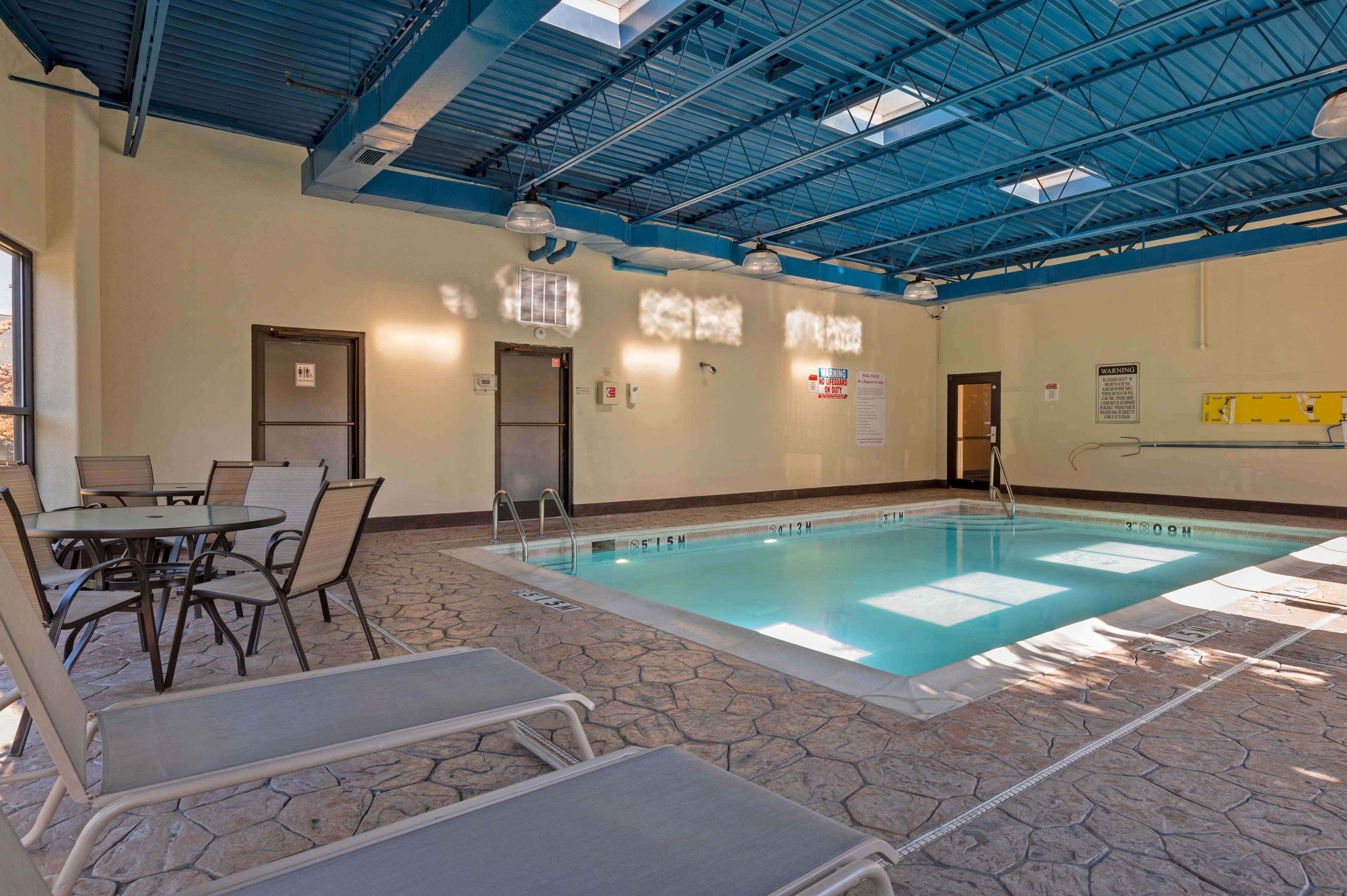 An indoor swimming pool with lounge chairs and tables, a tiled floor, and a blue ceiling.