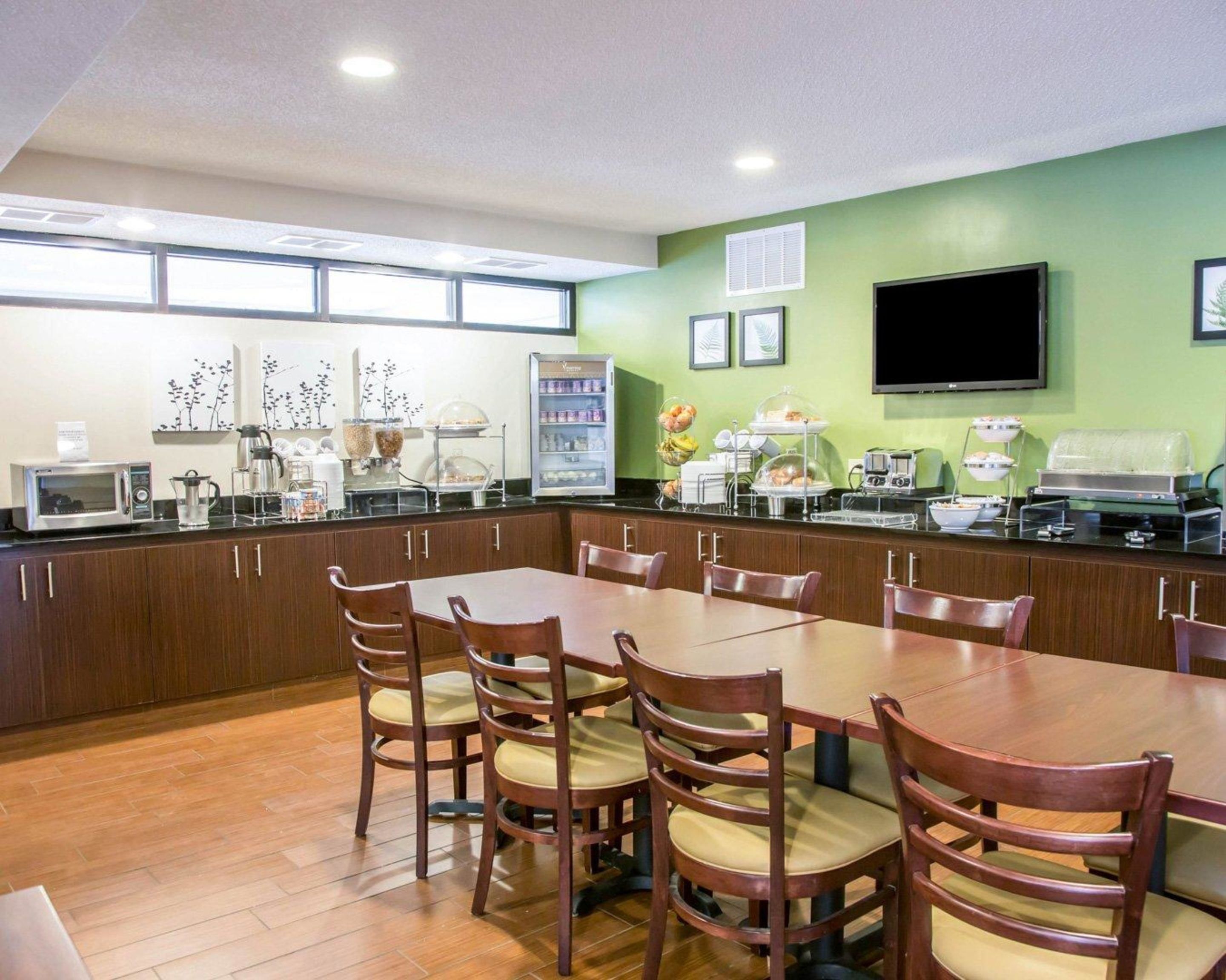 A dining area with a long table and chairs, a microwave, a coffee station, and a refrigerator with food items.