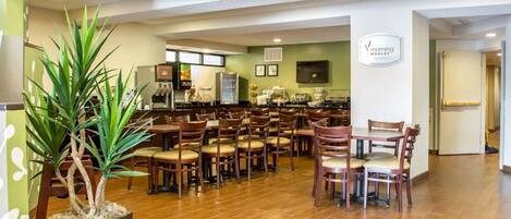 A spacious indoor area with multiple wooden tables and chairs, a coffee machine, and a refrigerator.
