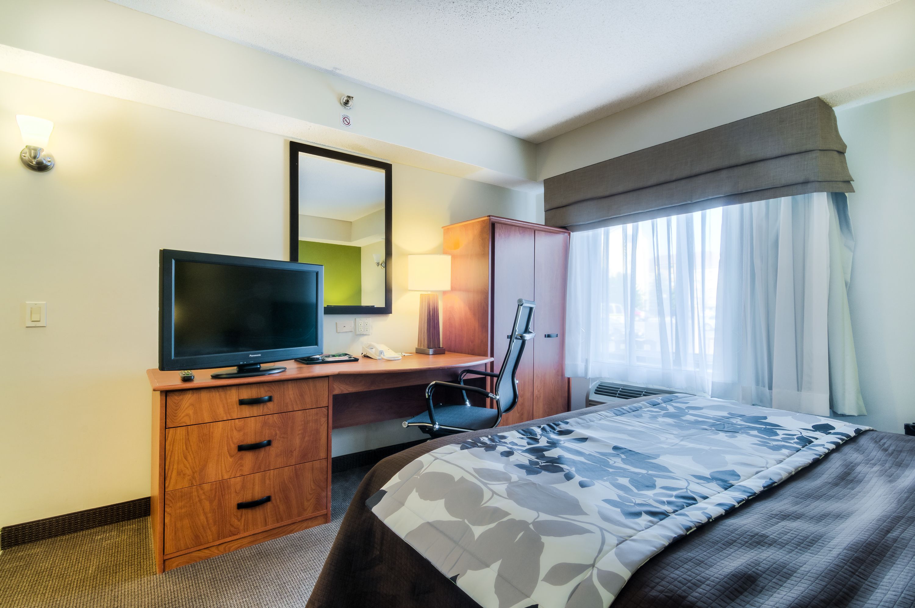 A hotel room with a bed, a desk with a television, a chair, a wardrobe, and a window with curtains.