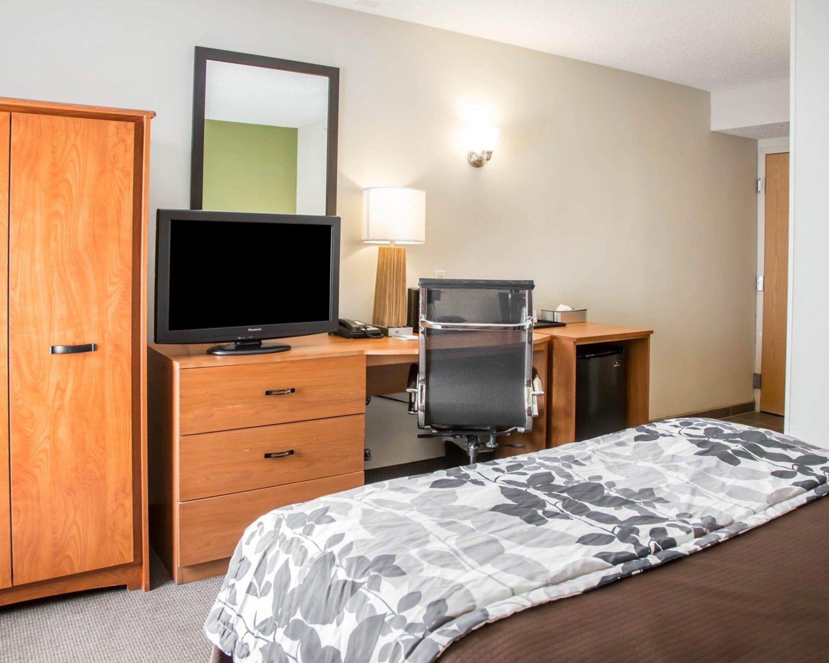 A hotel room with a wooden wardrobe, a desk with a computer, a television, and a bed with a floral bedspread.