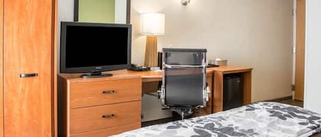 A hotel room with a wooden wardrobe, a desk with a computer, a television, and a bed with a floral bedspread.