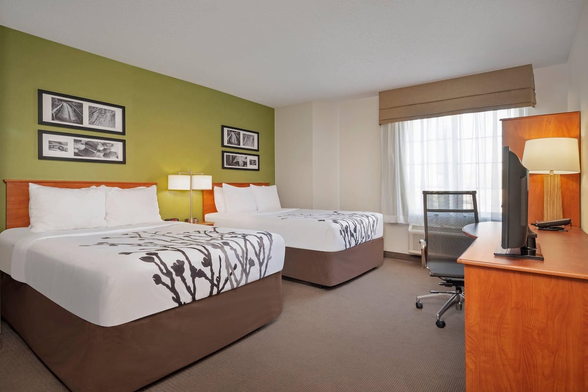 A hotel room with two beds, a desk with a computer, a chair, and framed pictures on the wall.