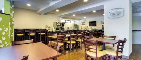 A spacious dining area with multiple tables and chairs, a kitchen in the background, and a logo on the wall.