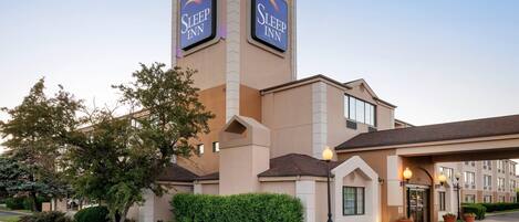 A Sleep Inn hotel with a prominent tower, a covered entrance, and a landscaped front yard.