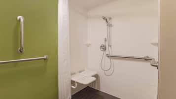 Baño con ducha, barras de apoyo, un banco blanco y una pared verde.