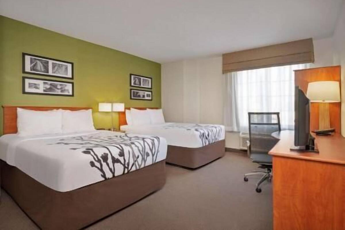 A hotel room with two beds, a desk, a chair, and a window with curtains.