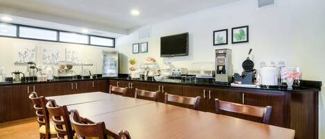 A spacious dining area with a long wooden table and chairs, equipped with a coffee machine and a microwave.